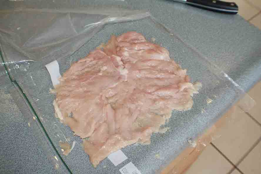 chicken breast pounded flat inside of plastic storage bag with plastic bag cut open on 3 sides and peeled back to show chicken