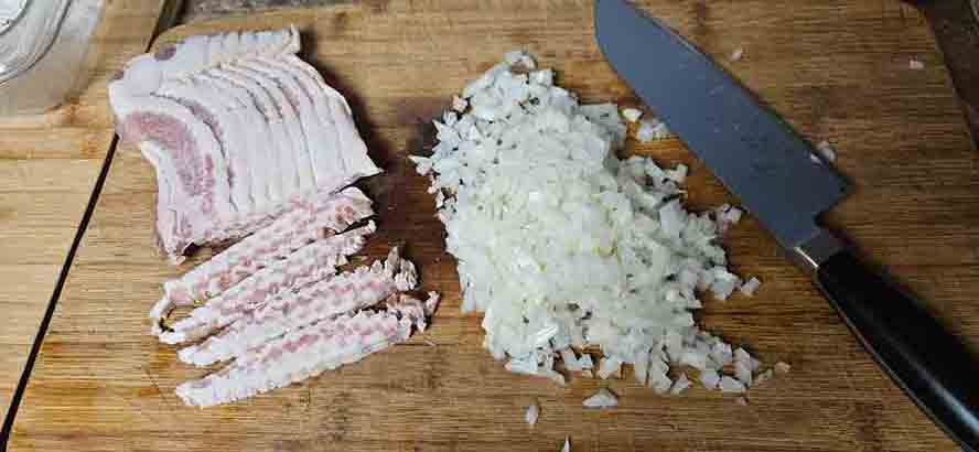 "Diced frozen bacon slices and chopped white onions prepared on a cutting board for frying."