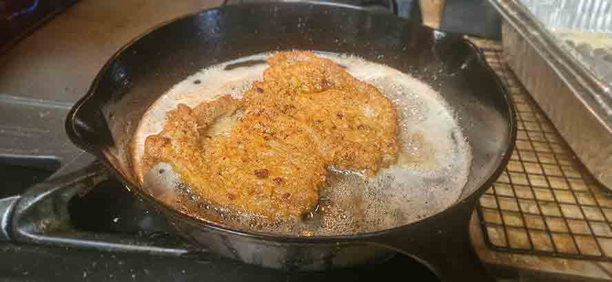 "Basting a frying Schnitzel with hot oil from the skillet to create the signature bubbly soufflé effect on the crust."