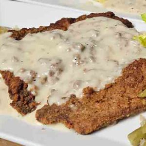 Crispy Chicken Fried Schnitzel served on a plate and smothered in thick, creamy white country gravy.
