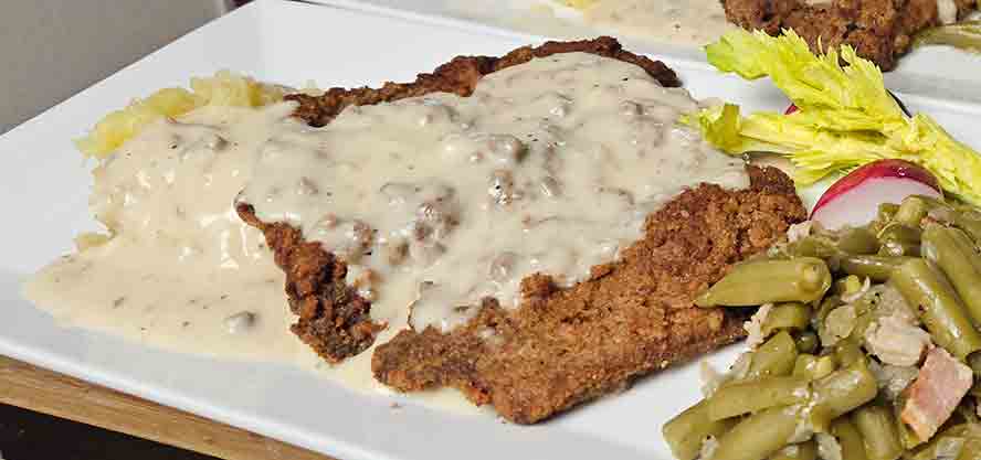 Crispy Chicken Fried Schnitzel served on a plate and smothered in thick, creamy white country gravy.