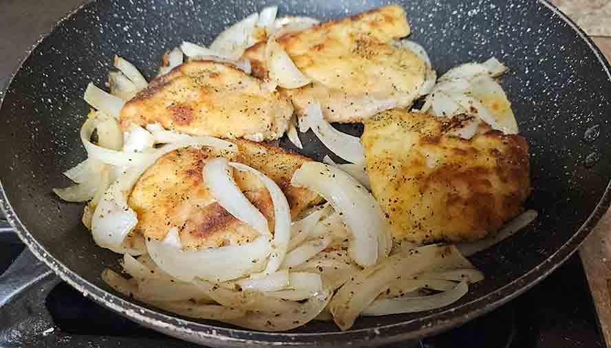 Pan-frying breaded Schnitzel in a skillet with softened, tender onions and golden-brown butter."