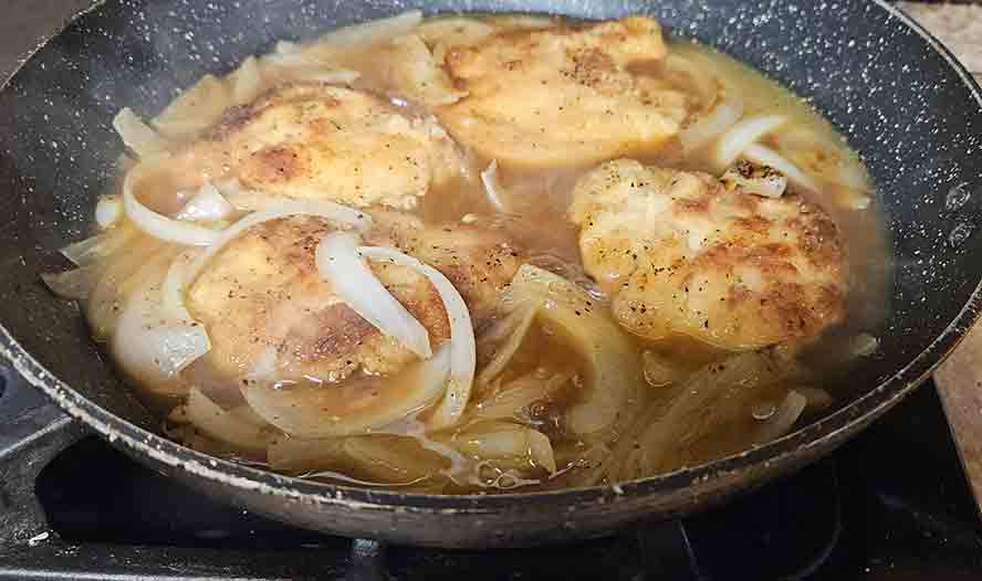 Schnitzel in a pan cooing with onions and beef stock. 