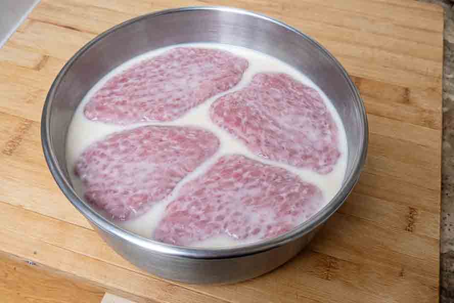 Soaking thin beef cutlets in a bowl of creamy buttermilk to tenderize the meat before breading