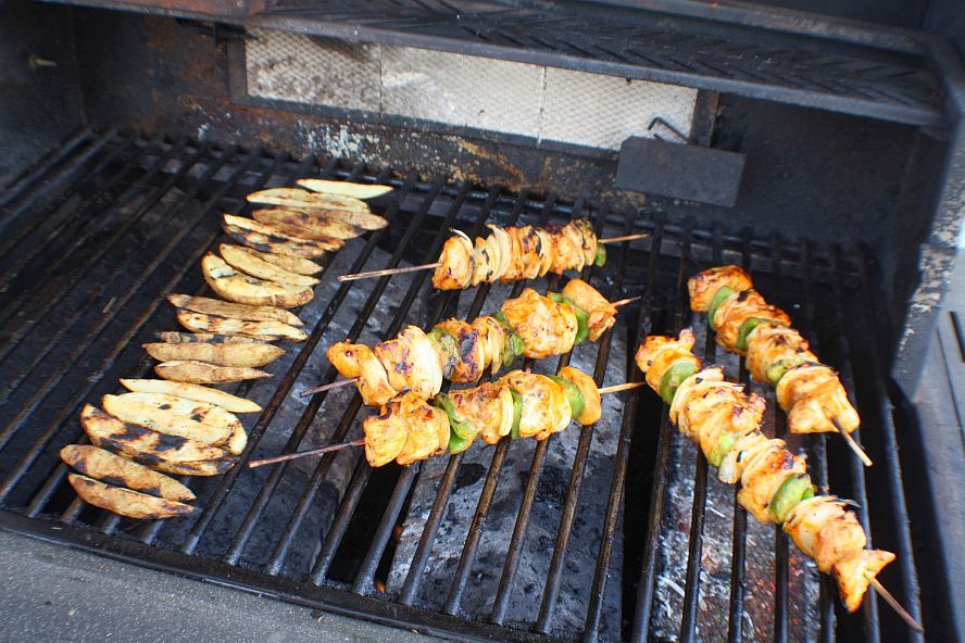 chicken-schaschlik-grill-wide.jpg multiple chicken skewers grilling alongside vegetables on outdoor grill