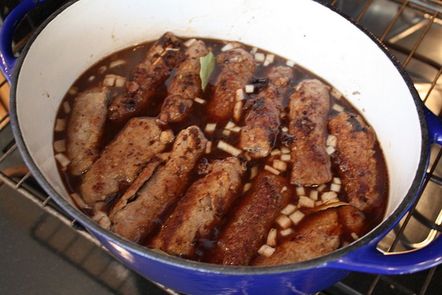 Rouladen simmering in beef stock and wine with onions