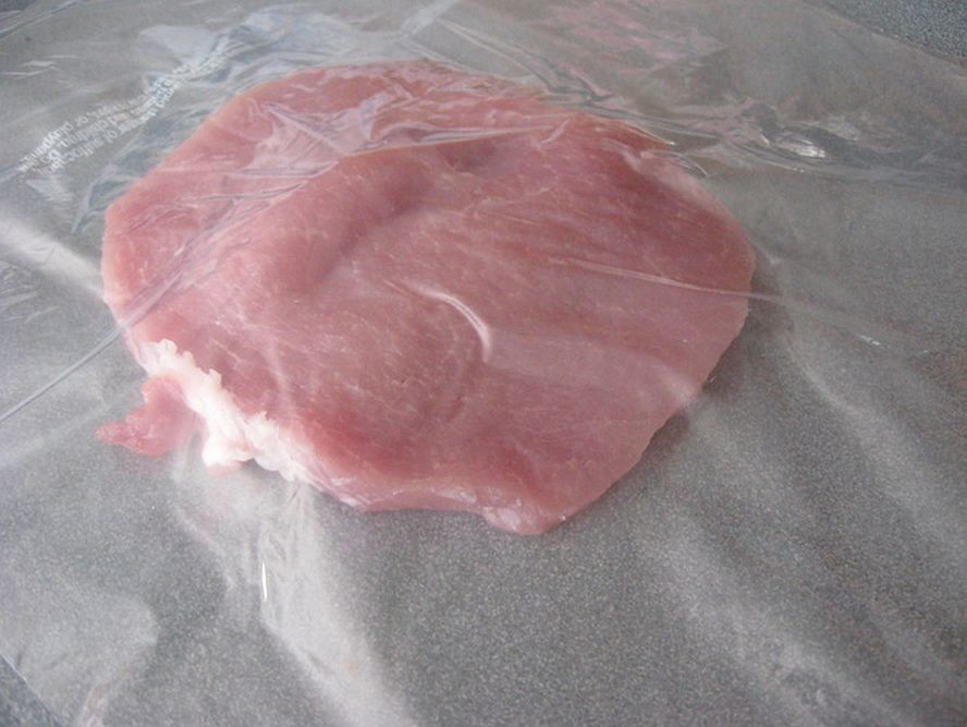 pork cutlet placed under plastic wrap ready for pounding