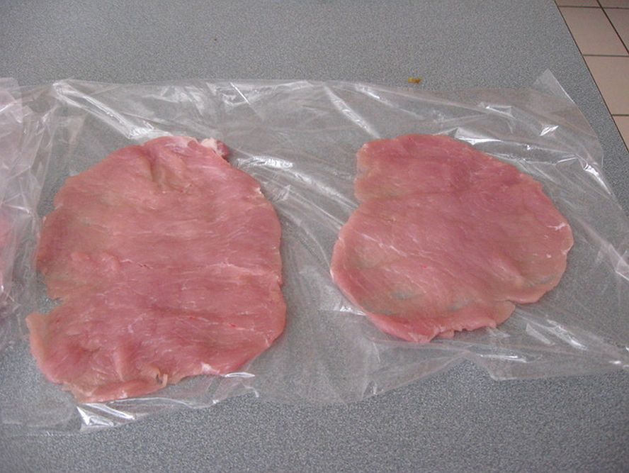 two pork cutlets under plastic wrap ready to be flattened