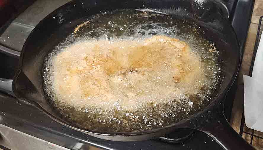 schnitzel frying in pan with bubbling hot oil