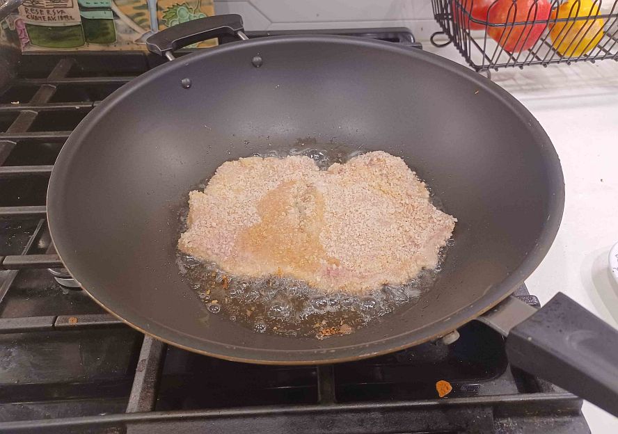 breaded schnitzel placed into hot oil for frying