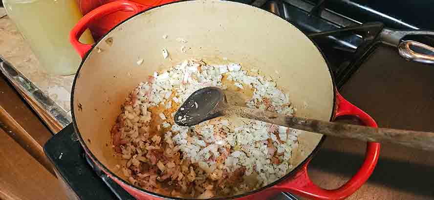 Bacon and chopped onion cooking together in a Dutch oven.