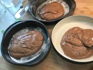 Chocolate cake batter divided among three prepared round cake pans.
