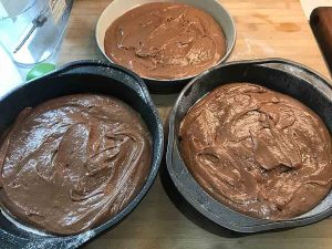 Three round cake pans filled evenly with chocolate cake batter and ready for baking.