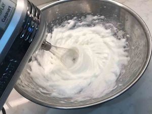 Egg whites whipped to a thick, fluffy consistency in a stainless steel bowl.