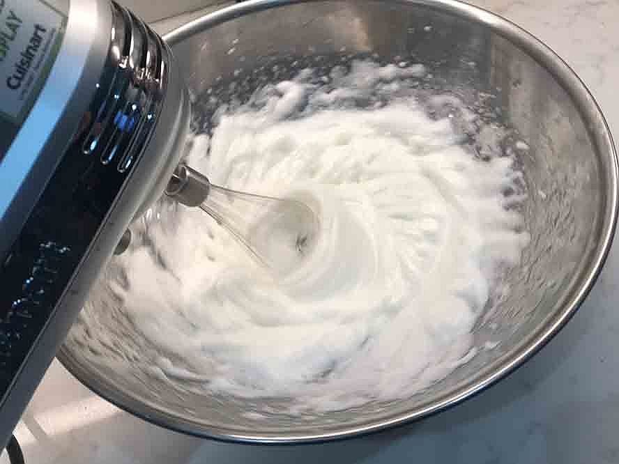 Egg whites whipped to a thick, fluffy consistency in a stainless steel bowl.