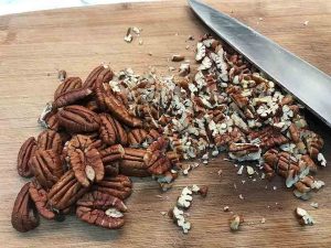 Pecans being chopped into small pieces on a wooden cutting board.