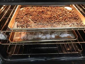 Chopped pecans being toasted in a baking pan in the oven.