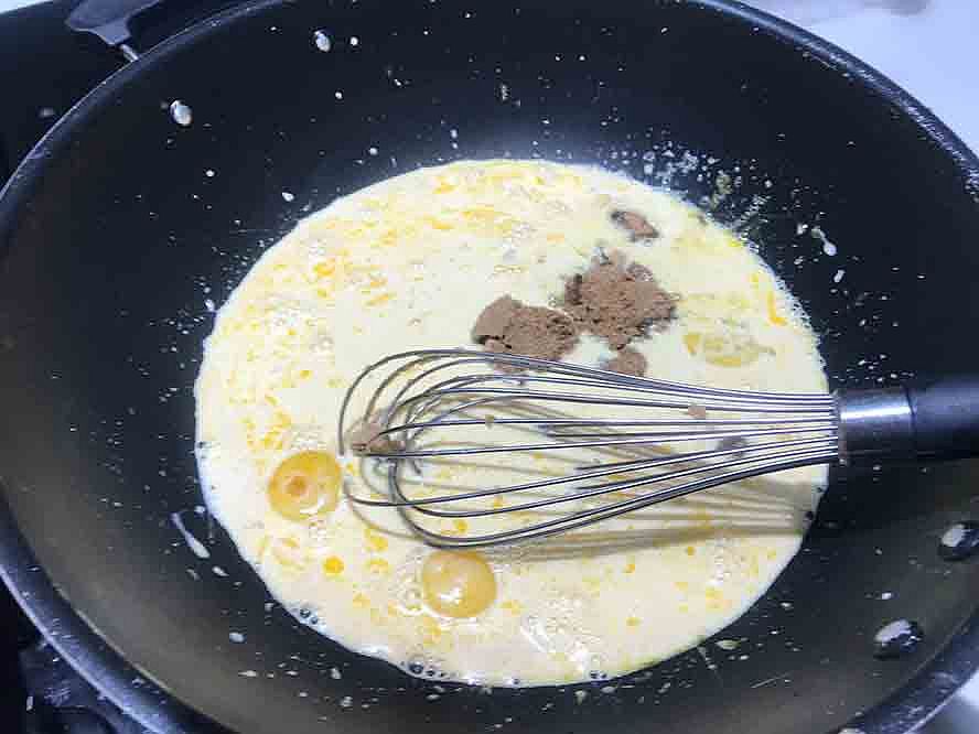 Milk, egg yolks, sugar, and chocolate ingredients being whisked together in a saucepan.
