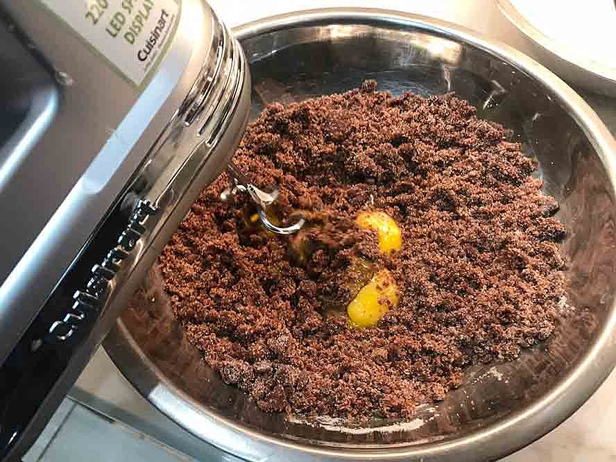 Eggs being added to the chocolate cake mixture while it is being mixed.