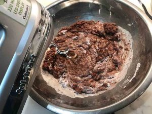 Chocolate cake batter being mixed with the eggs and other ingredients in a stainless steel bowl.