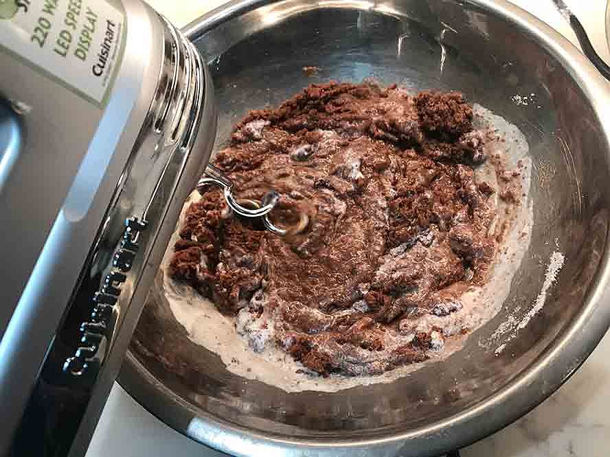 Chocolate cake batter being mixed with the eggs and other ingredients in a stainless steel bowl.