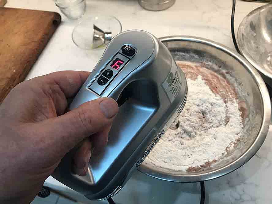 Chocolate cake batter being mixed with the eggs and other ingredients in a stainless steel bowl.